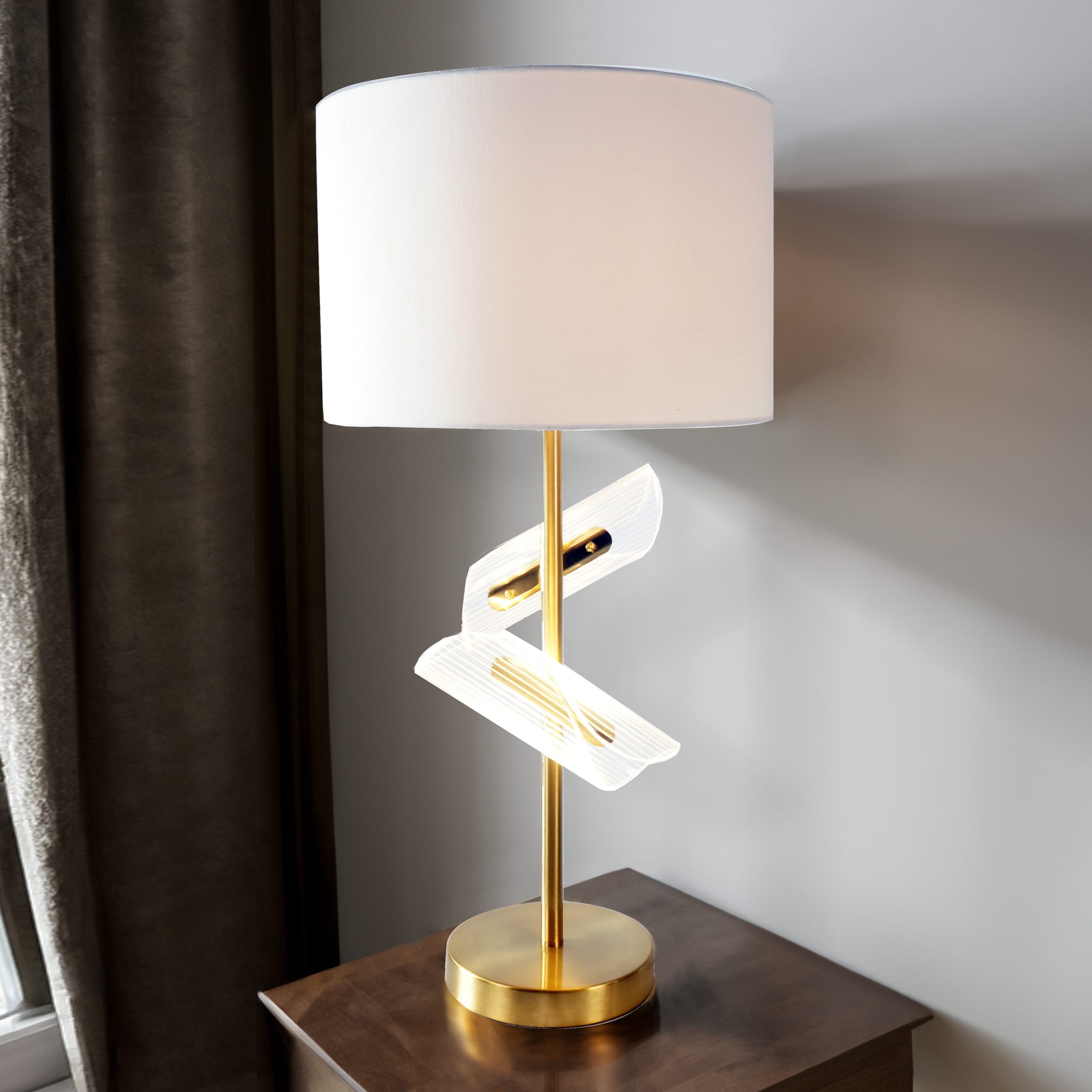 The #6248T "Modern Gold" Table Lamp (Set of 2) features a gold base and pole, sculptural white accent, and large white drum shade. Shown on a wooden side table by a window with dark curtains.