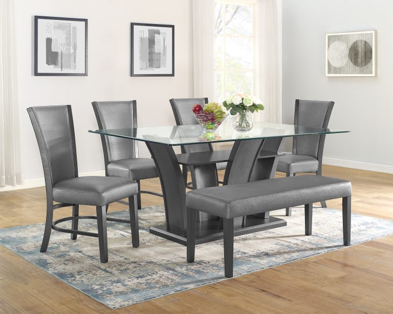Modern dining room with a glass table, four gray upholstered chairs, and a matching bench on a blue-patterned rug. Light, airy ambiance.